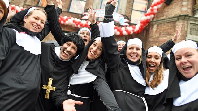 Menschen in Nonnen- und Mönchskostümen lachen und posieren für ein Foto.