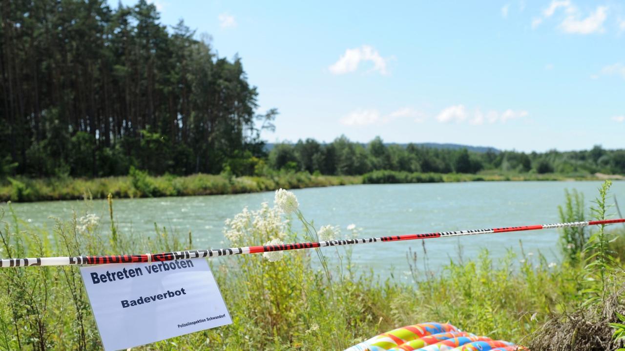 Ein Schild mit der Aufschrift "Betreten verboten Badeverbot" neben einer Luftmatratze an einem See. Ein Schild mit der Aufschrift "Betreten verboten Badeverbot" neben einer Luftmatratze an einem See.