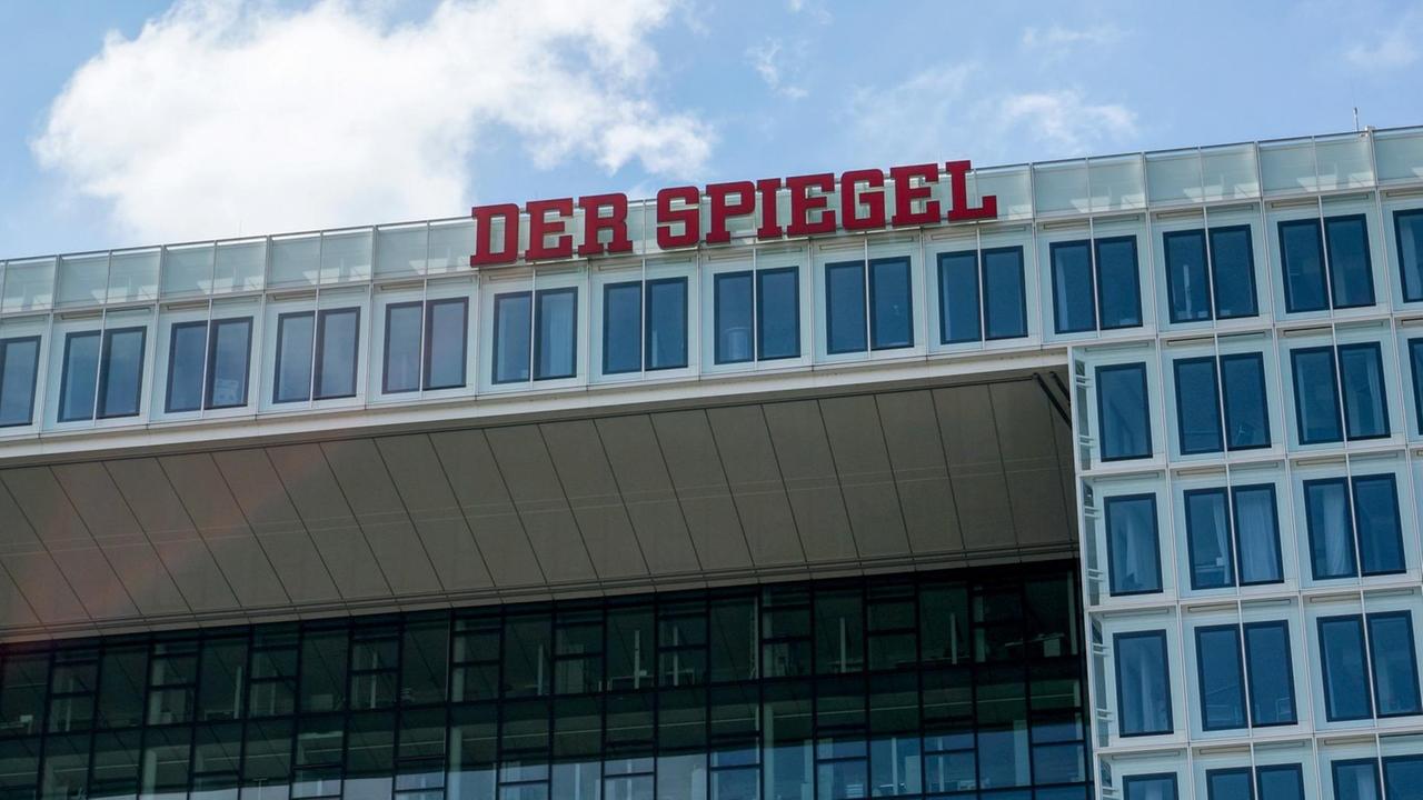Das Gebäude von unten im Anschnitt vor blauem Himmel mit Wolken fotografiert. Im Bildzentrum die roten Neon-Buchstaben "Der Spiegel".