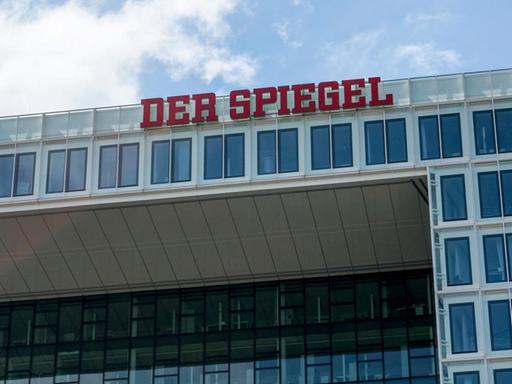 Das Gebäude von unten im Anschnitt vor blauem Himmel mit Wolken fotografiert. Im Bildzentrum die roten Neon-Buchstaben "Der Spiegel".