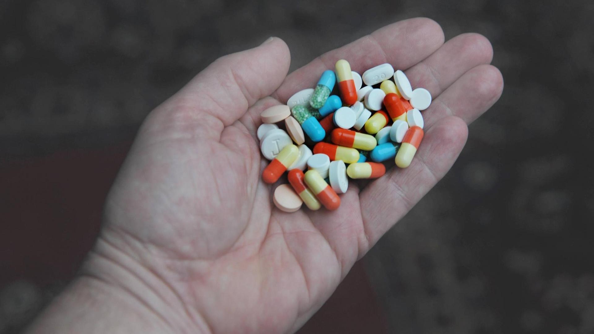 In einer Hand liegen viele verschiedenfarbige Tabletten. In einer Hand liegen viele verschiedenfarbige Tabletten.