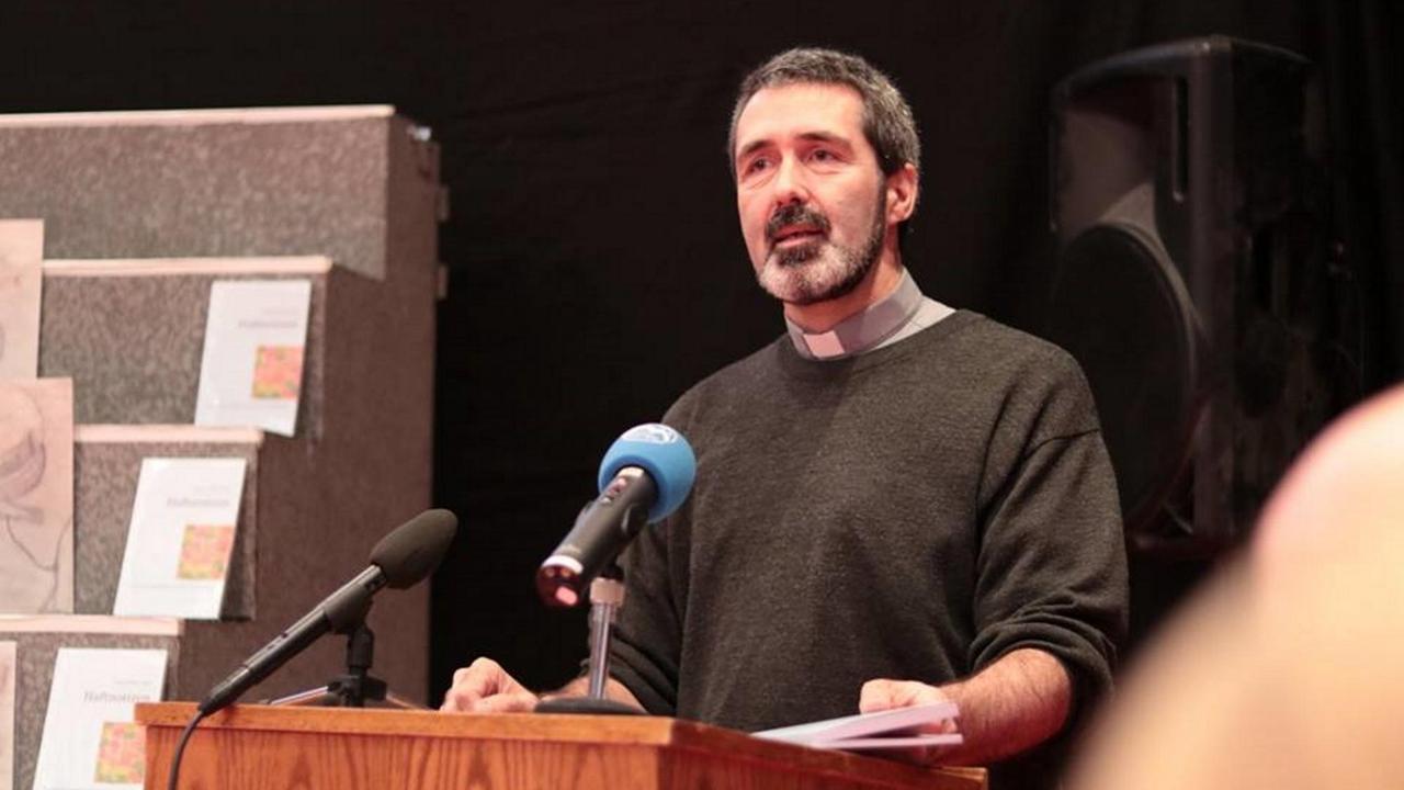 Seelsorger Thomas Marin steht in dunklem Sweatshirt an einem Rednerpult und spricht in ein Mikrofon.
