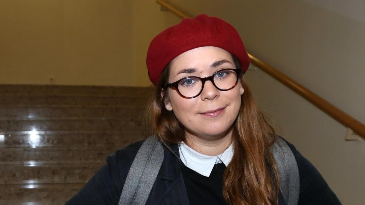 Stefanie Sargnagel mit Brille und roter Mütze im Treppenaufgang.