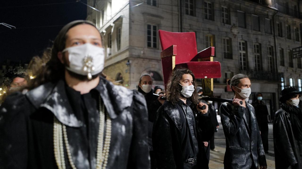 Demonstrierende tragen einen rot bezogenen Theatersessel durch die Straßen