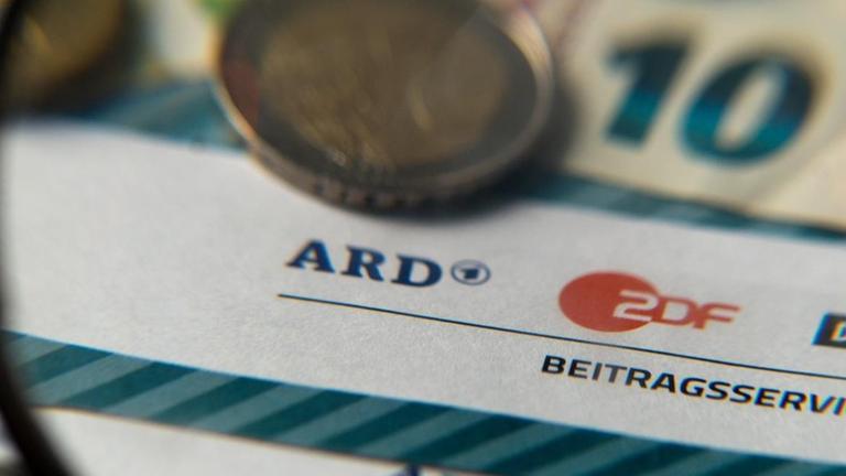 Auf einem Tisch liegt Münzgeld auf Formularen für Bürgerinnen und Bürger zu den Rundfunkbeiträgen ARD, ZDF und DRadio.