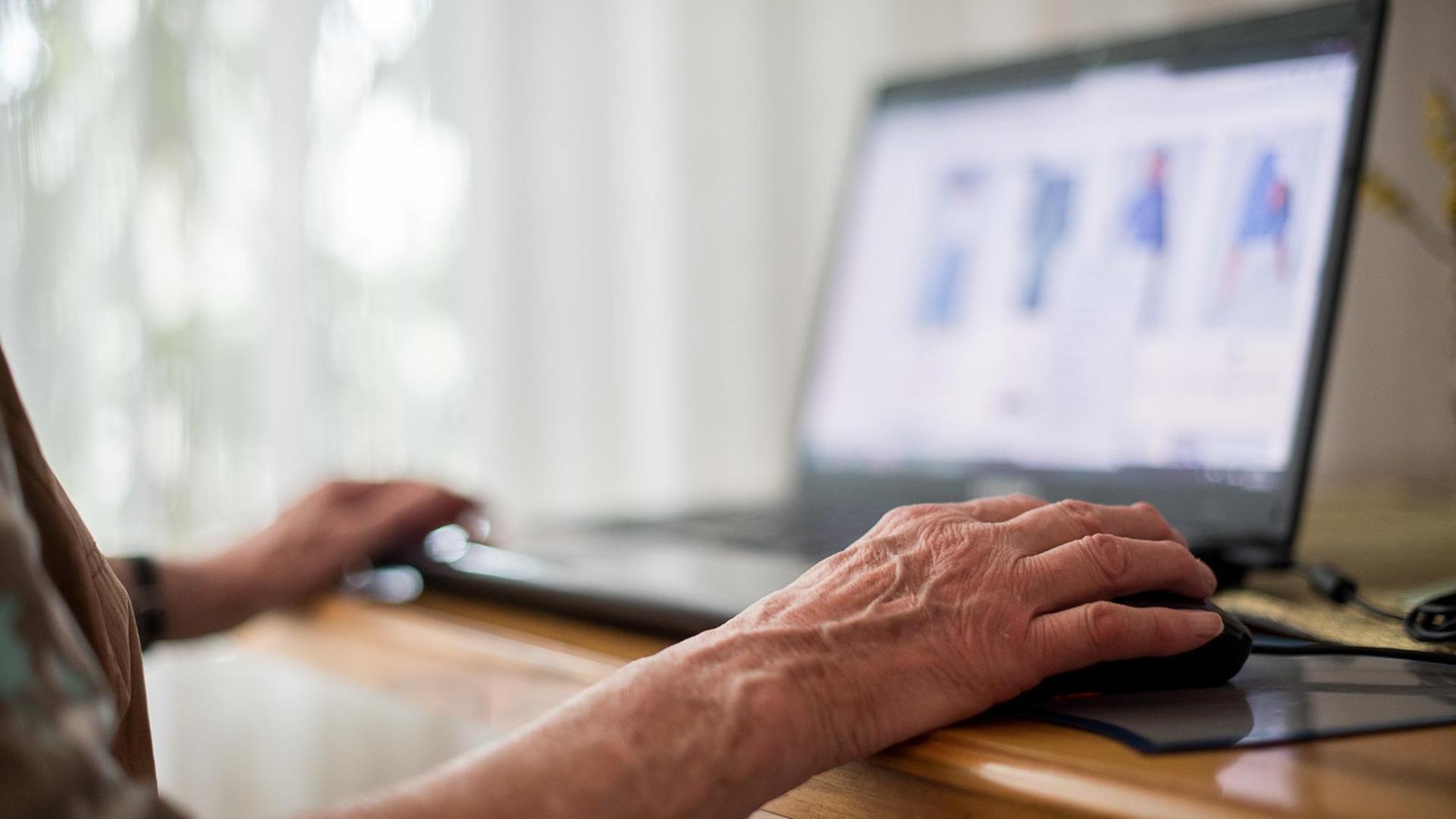 Eine Seniorin sitzt an ihrem Laptop und hat ihre Hand auf einer Maus liegen Eine Seniorin sitzt an ihrem Laptop und hat ihre Hand auf einer Maus liegen
