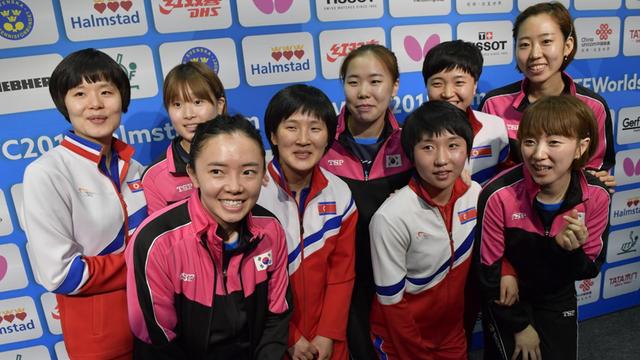 Die Mitglieder der nordkoreanischen und südkoreanischen Tischtennismannschaften stehen nach der Entscheidung, ein gemeinsames Team zu bilden, zusammen vor einer Sponsorenwand.