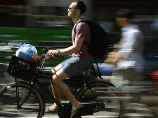 Ein Mann transport in seinem Fahrradkorb vorne am Lenker seine Einkäufe, während entlang einer der Amsterdamer Grachten fährt.