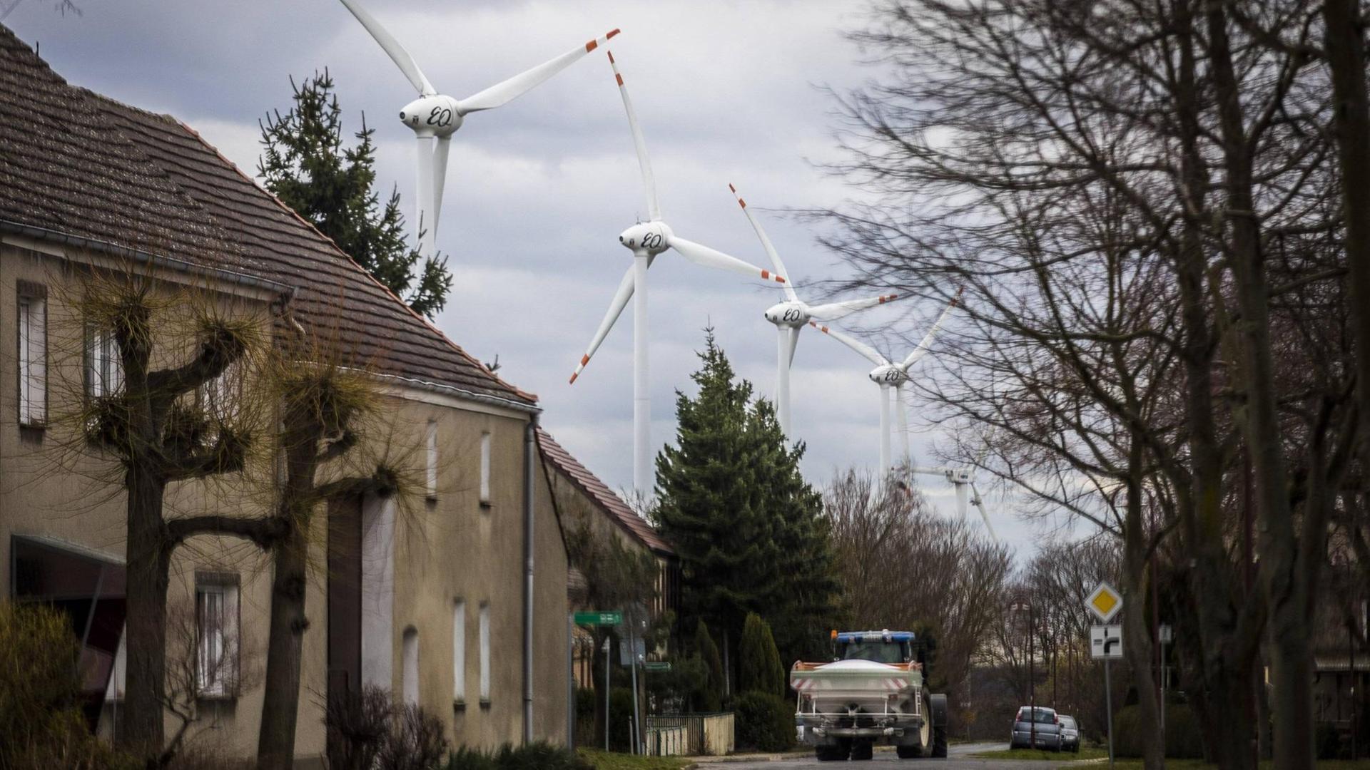 Blick auf eine Dorfstraße in Feldheim (Brandenburg) Auf der Straße fährt ein LKW, links schmucklose grau-braun gestrichene Häuser, im Hintergrund die Windräder eines Windparks. Blick auf eine Dorfstraße in Feldheim (Brandenburg) Auf der Straße fährt ein LKW, links schmucklose grau-braun gestrichene Häuser, im Hintergrund die Windräder eines Windparks.