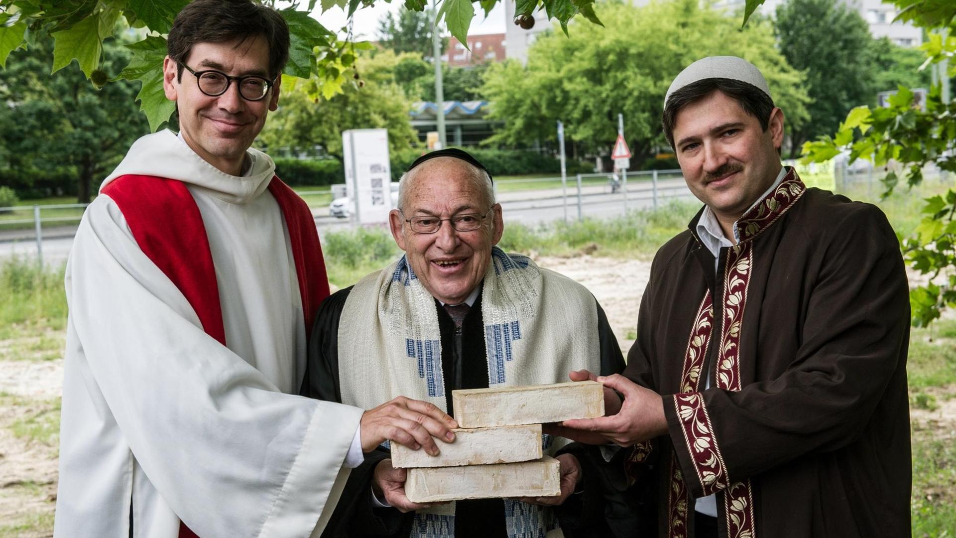 Der Pfarrer Gregor Hohberg, der Rabbiner Tovia Ben-Chorin und der Imam Kadir Sanci halten auf dem Petriplatz gemeinsam drei Ziegelsteine in den Händen.