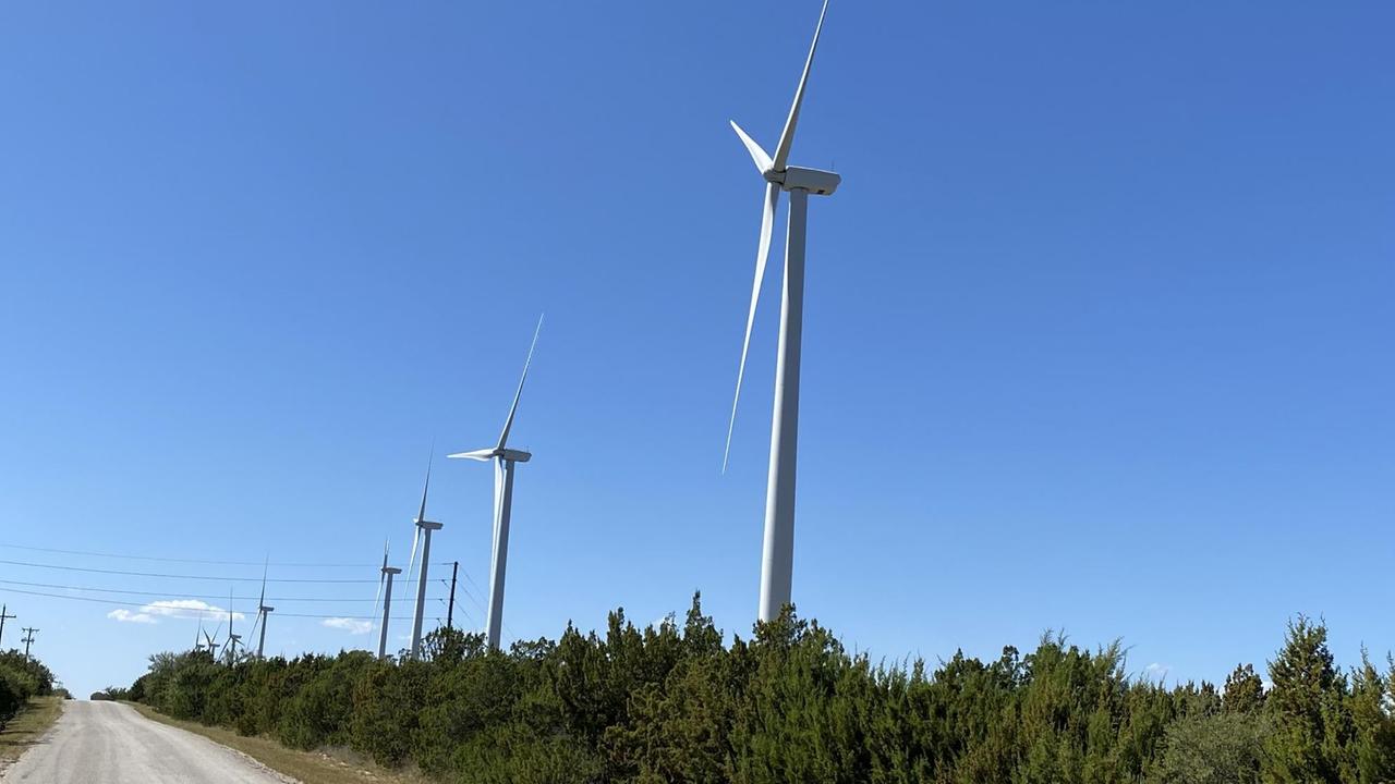 Windräder stehen im Grünen in einer Reihe eine Straße entlang. Windräder stehen im Grünen in einer Reihe eine Straße entlang.