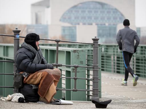 Udo, ein Obdachloser, sitzt in Berlin an der Spree im Regierungsviertel und bittet um Unterstützung.