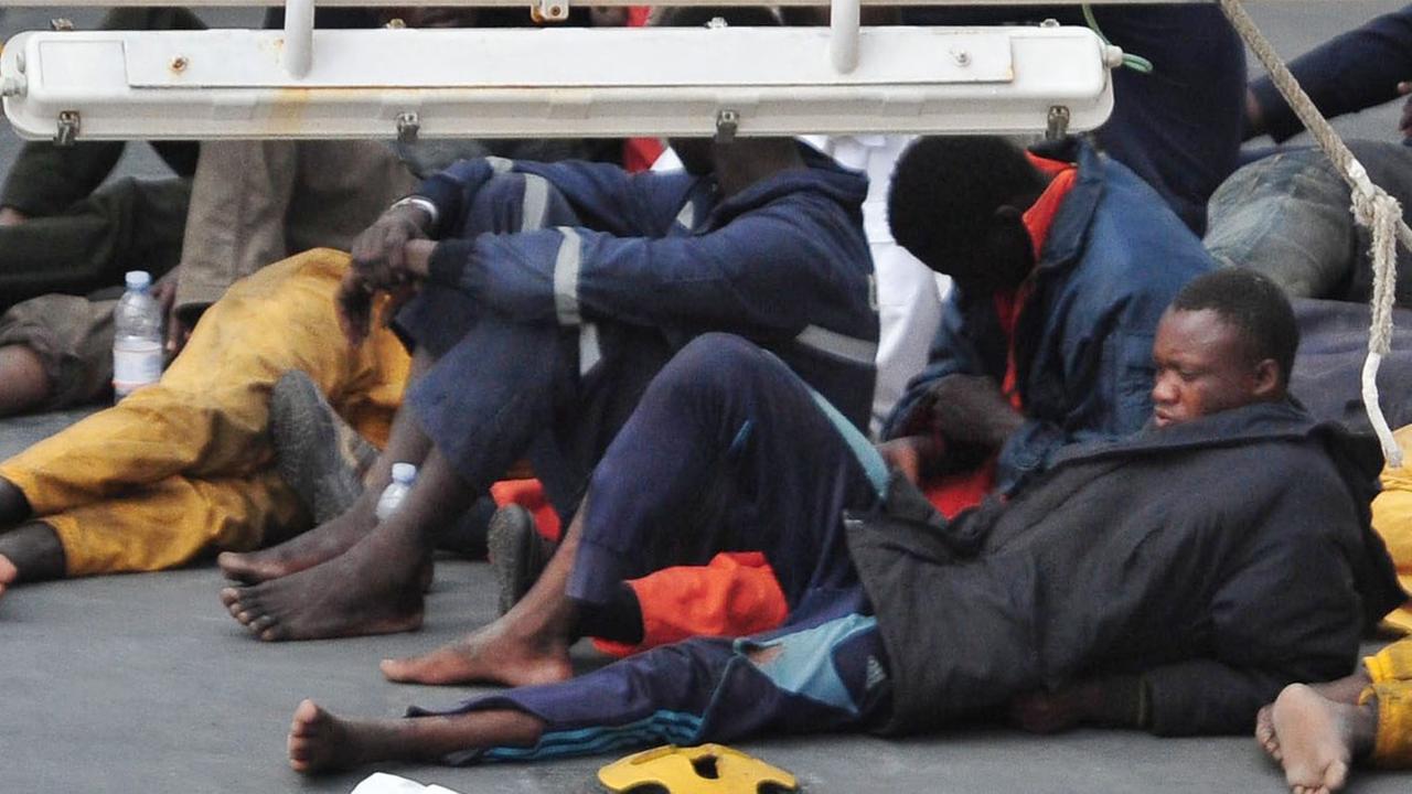 Auf dem Deck eines Schiffs der italienischen Küstenwache liegen gerettete Flüchtlinge. Auf dem Deck eines Schiffs der italienischen Küstenwache liegen gerettete Flüchtlinge.