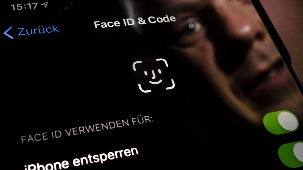 Symbolfoto: Ein Mann spiegelt sich in einem Apple Smartphone auf dem der Schriftzug Face ID zu sehen ist.