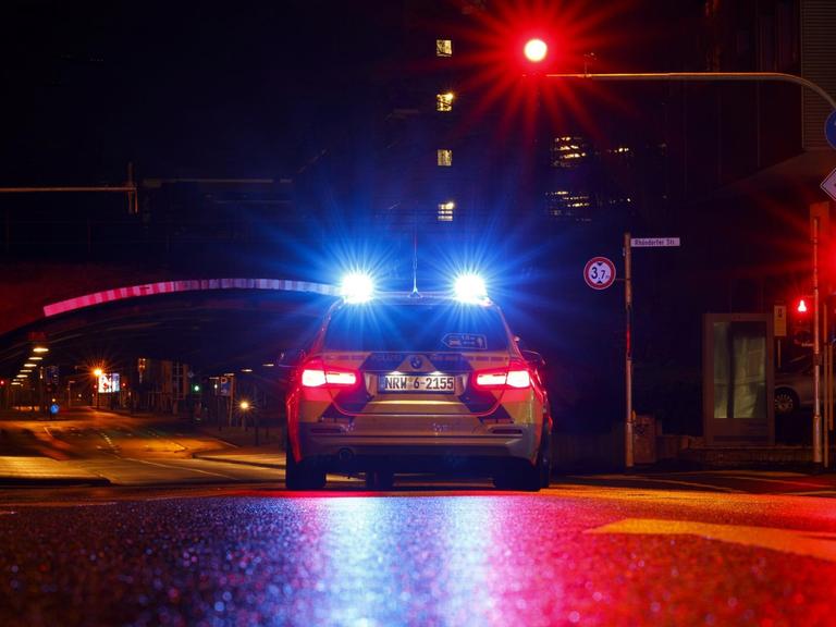 Ein Polizeiauto steht in der Nacht an einer roten Ampel.