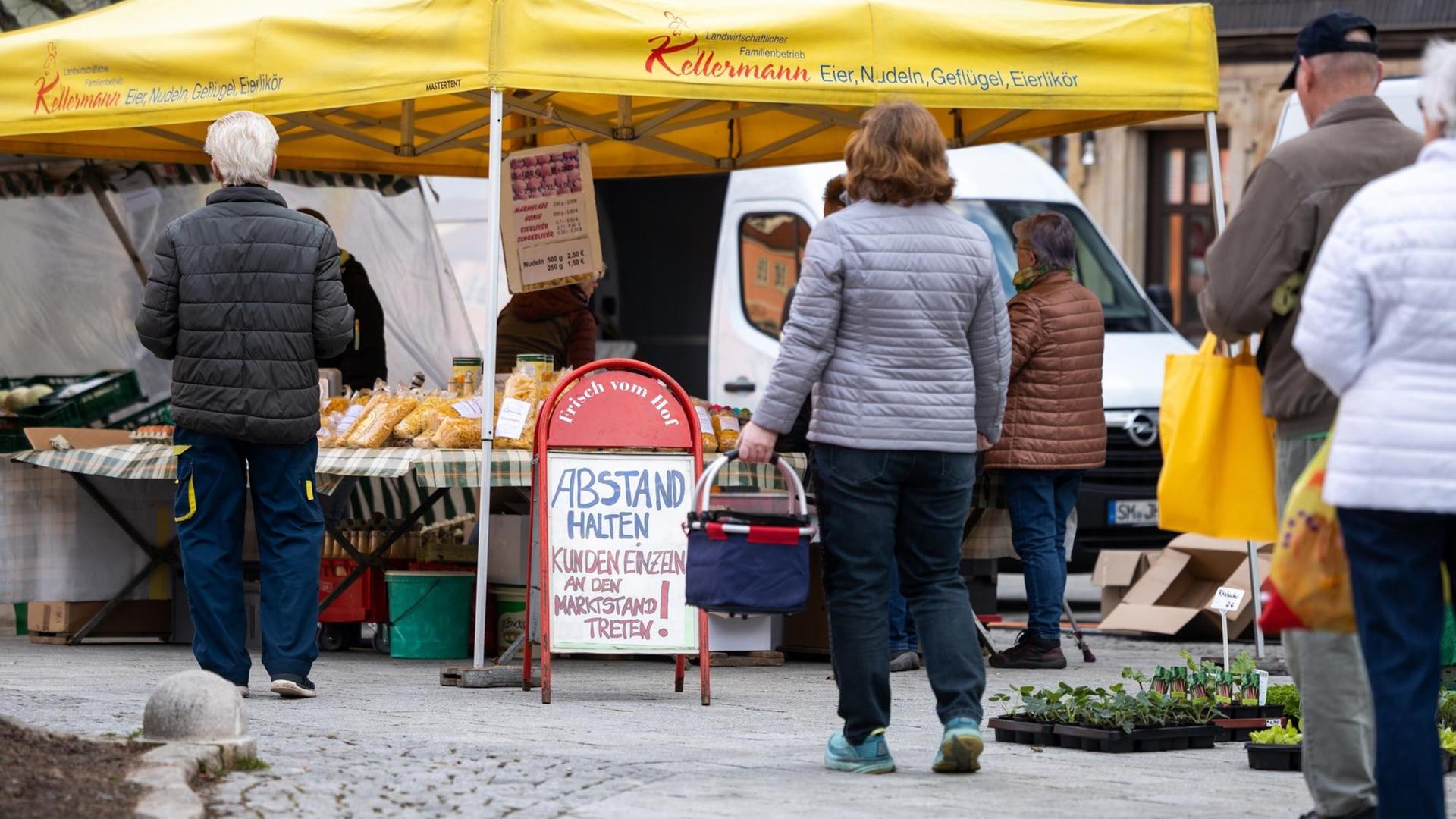 Ein Schild mit der Aufschrift "Abstand halten" steht vor einem Marktstand auf einem Wochenmarkt.