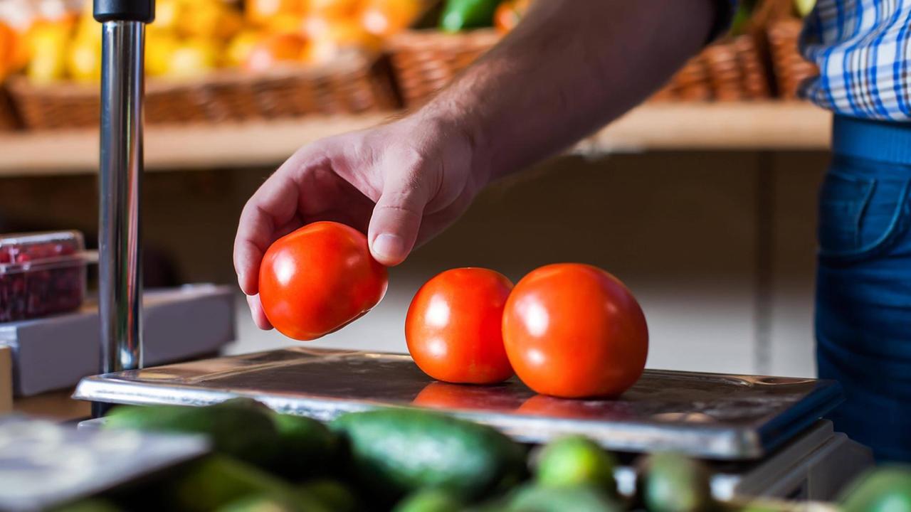Eine Person legt in einem Supermarkt Tomaten auf eine Waage. Eine Person legt in einem Supermarkt Tomaten auf eine Waage.