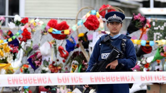Eine Polizistin steht vor dem abgesperrten Tatort des Terroranschlags in Christchurch, hinter ihr sind zahlreiche niedergelegte Blumen zu sehen.