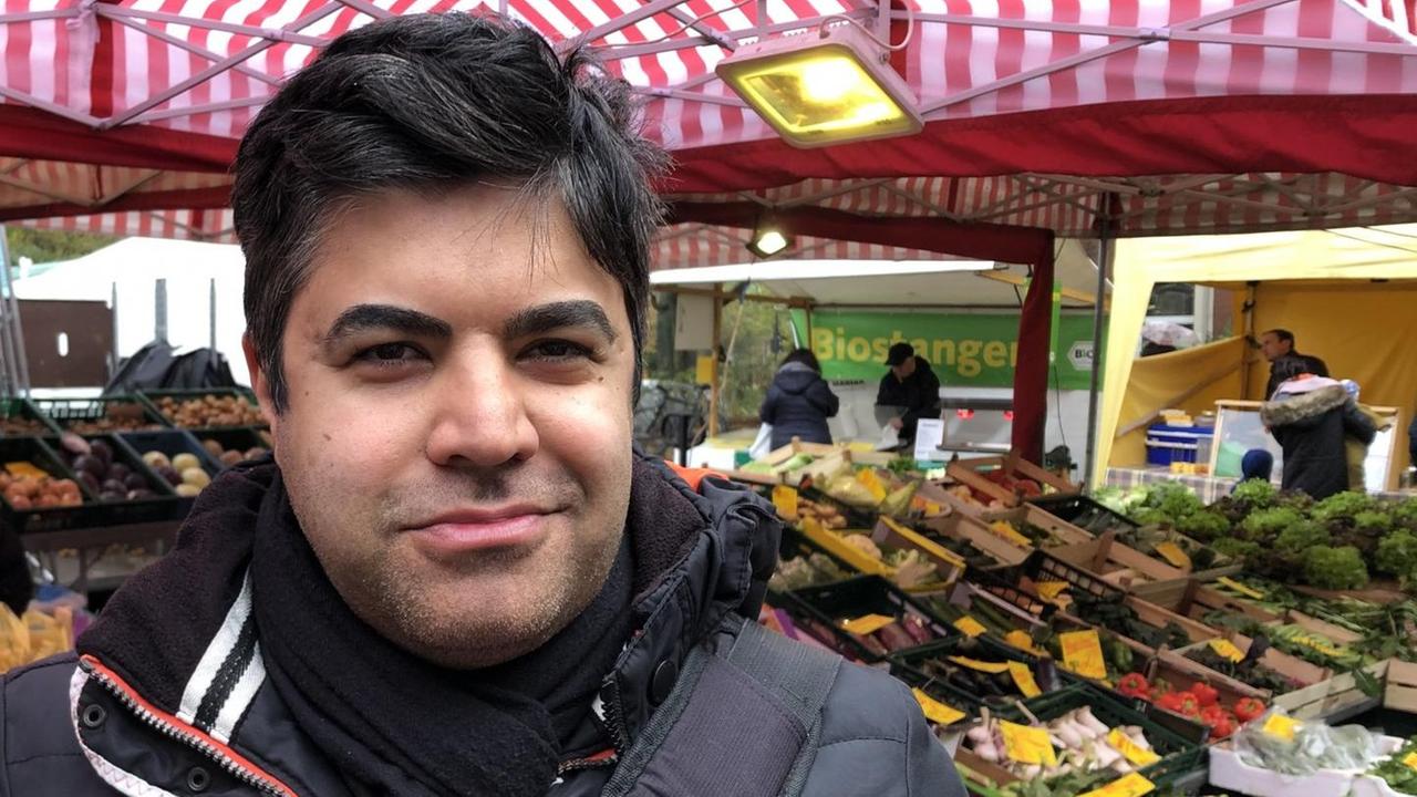 Ein Mann steht vor einem Marktstand mit Gemüse. Ein Mann steht vor einem Marktstand mit Gemüse.