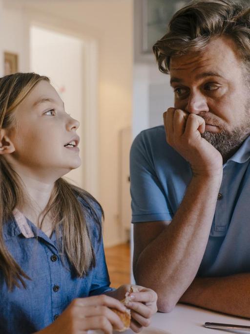 Eine Tochter erklärt am Küchentisch dem Vater etwas, dieser grübelt etwas verzweifelt darüber nach.