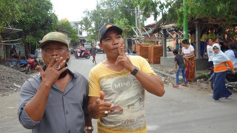 Zwei Männer stehen auf einer Straße in Indonesien und rauchen demonstrativ.