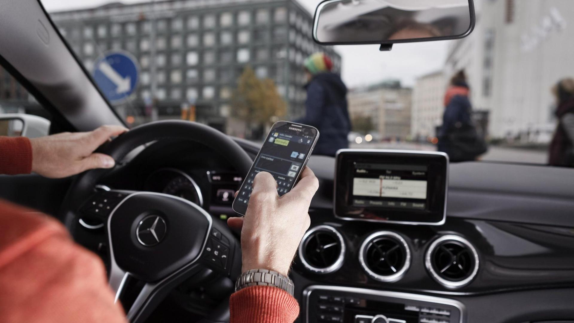 Blick von der Rückbank auf den Fahrer eines Autos, der ein Mobiltelefon in der rechten Hand hat. Blick von der Rückbank auf den Fahrer eines Autos, der ein Mobiltelefon in der rechten Hand hat.