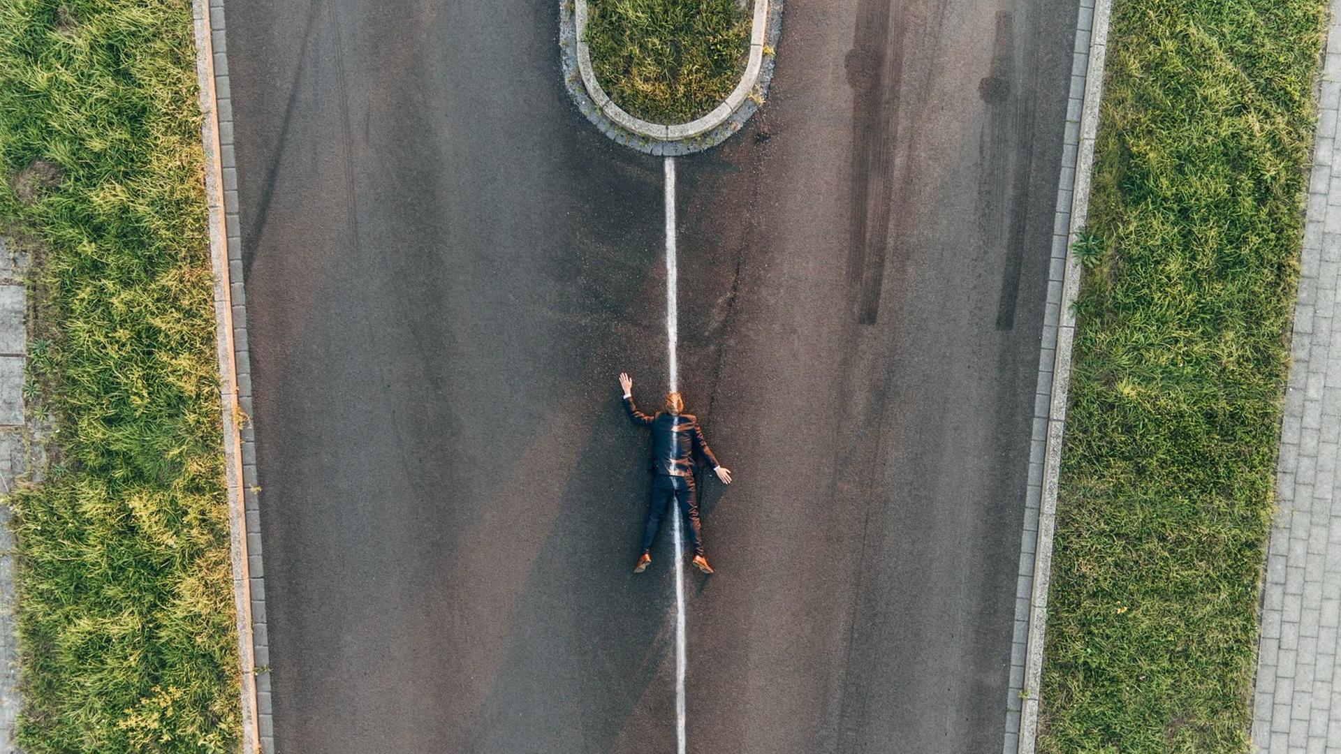 Ein Mann liegt auf einer zweigeteilten Straße, über ihn ist eine Straßenbegrenzung gezogen. Er sieht wie überfahren aus. Ein Mann liegt auf einer zweigeteilten Straße, über ihn ist eine Straßenbegrenzung gezogen. Er sieht wie überfahren aus.