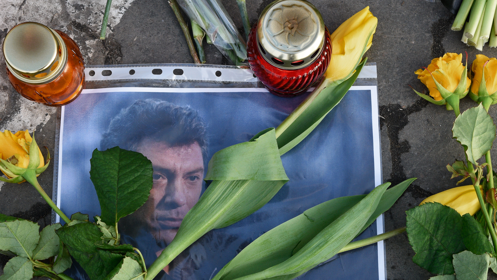Ein Bild des russischen Oppositionspolitikers Nemzow liegt auf der Straße am Tatort in Moskau; es wird von zwei Kerzen beschwert. Darauf und daneben liegen Blumen.