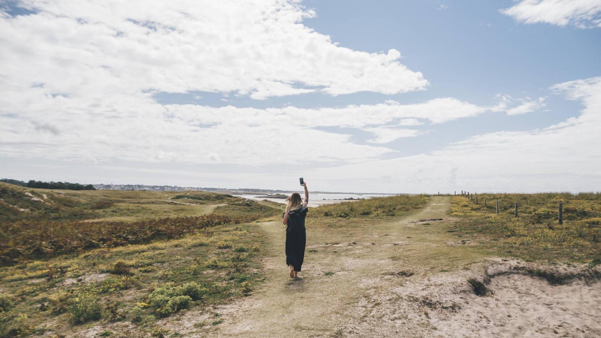 Eine Frau hält in der Natur in der Bretagne ihr Smartphone in die Luft. (Symbolfoto)