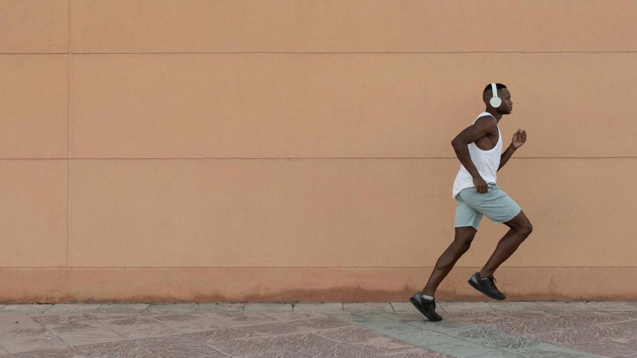 Ein Läufer mit Kopfhörern rennt vor einer gelben Mauer entlang.