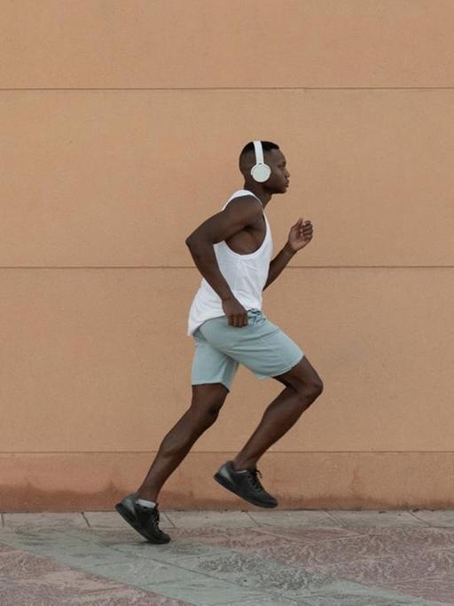Ein Läufer mit Kopfhörern rennt vor einer gelben Mauer entlang.