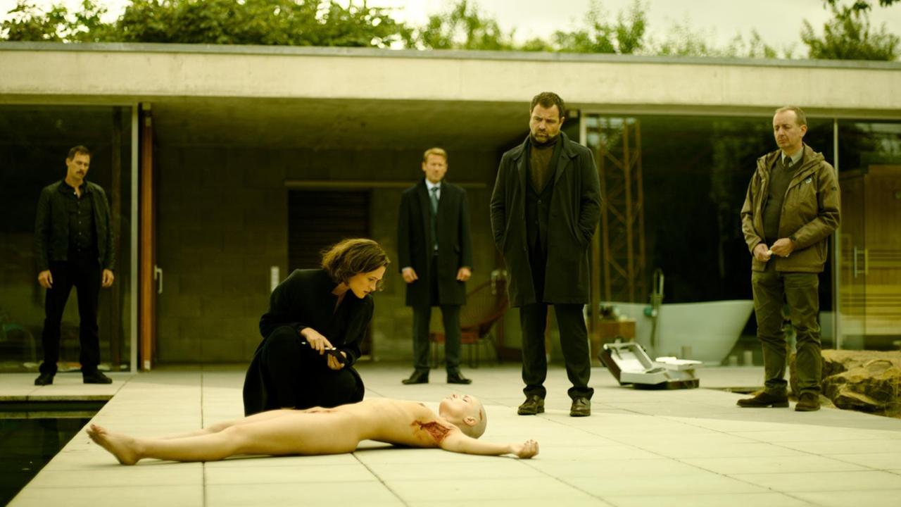 Die Ermittler Brettschneider (Marc Hosemann) und Köhler (Juergen Maurer) sowie Staatsanwalt Grünberg (Wotan Wilke Möhring) untersuchen mit Profilerin Nadja Simon (Friederike Becht) den Tatort und das Opfer: Eine Leiche liegt vor dem Eingang eines Bungalows Die Ermittler Brettschneider (Marc Hosemann) und Köhler (Juergen Maurer) sowie Staatsanwalt Grünberg (Wotan Wilke Möhring) untersuchen mit Profilerin Nadja Simon (Friederike Becht) den Tatort und das Opfer: Eine Leiche liegt vor dem Eingang eines Bungalows