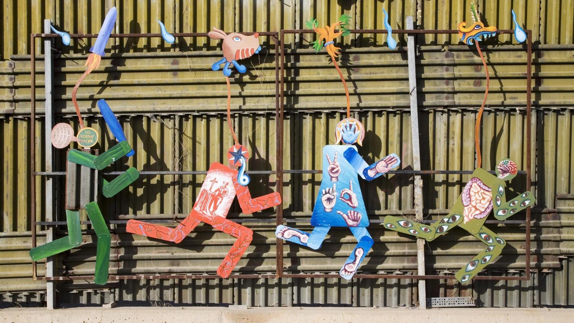 Kunstwerk auf der mexikanischen Seite des Grenzzauns, der die USA von Mexiko trennt, zeigt einen US-Grenzschutzpolizisten, der mit Schlagstock mehrere flüchtende Personen verfolgt, aufgenommen in Nogales, Sonora, Mexiko