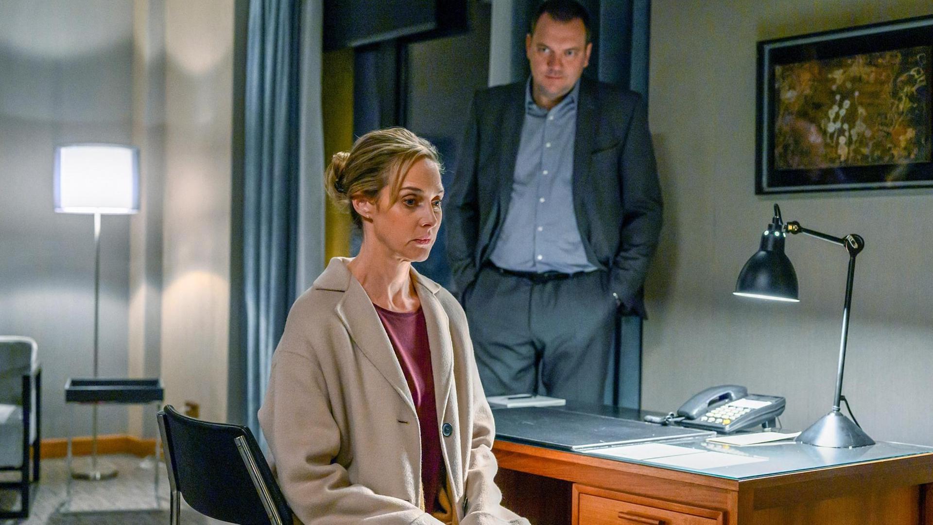 Szene aus dem Fernsehfilm "Das Verhör in der Nacht". Thomas (Charly Hübner) wartet auf eine Antwort von Judith (Sophie von Kessel), die auf einem Schreibtischstuhl sitzend in Gedanken versunken ist.