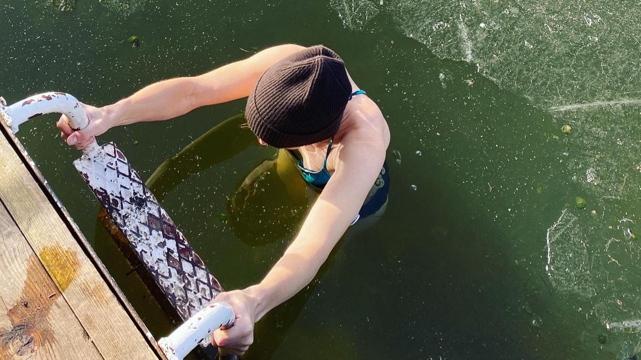 Eine Frau beim Eisbaden im See; nach dem Bad steigt sie die Leiter hoch, auf dem Wasser ist eine dünne Eisschicht zu sehen. Eine Frau beim Eisbaden im See; nach dem Bad steigt sie die Leiter hoch, auf dem Wasser ist eine dünne Eisschicht zu sehen.