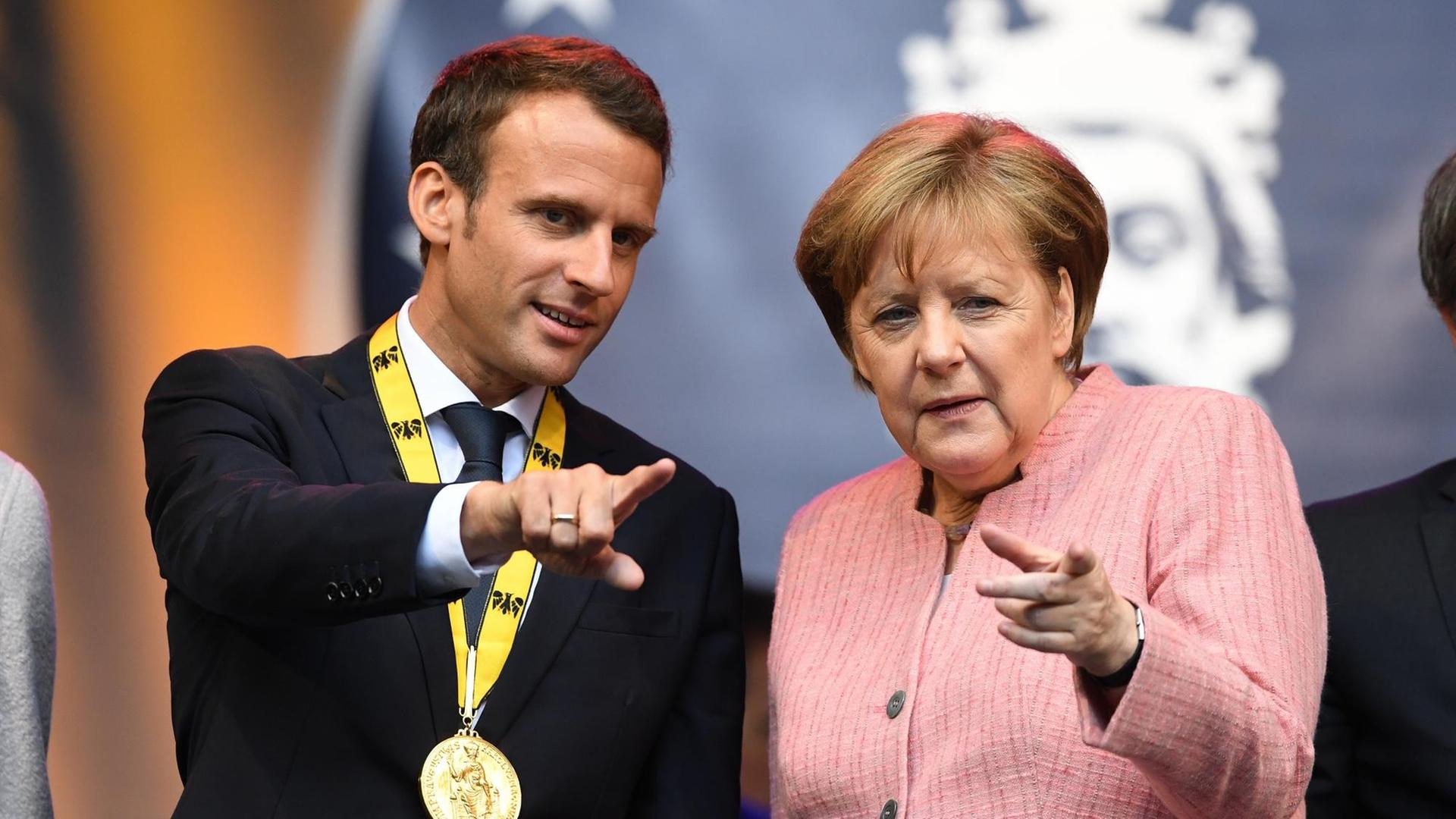 Bundeskanzlerin Angela Merkel (CDU), und der französische Staatspräsident Emmanuel Macron stehen nach der Verleihung des Karlspreises auf einer Tribüne.