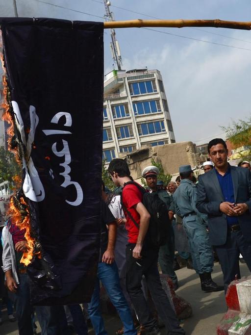 Zu sehen sind Menschen, die eine Fahne der Terrormiliz IS verbrennen.