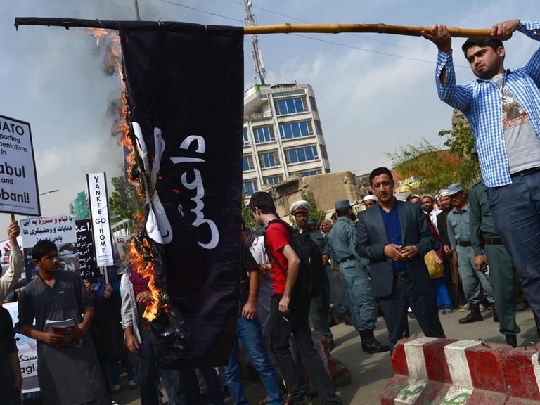 Zu sehen sind Menschen, die eine Fahne der Terrormiliz IS verbrennen.
