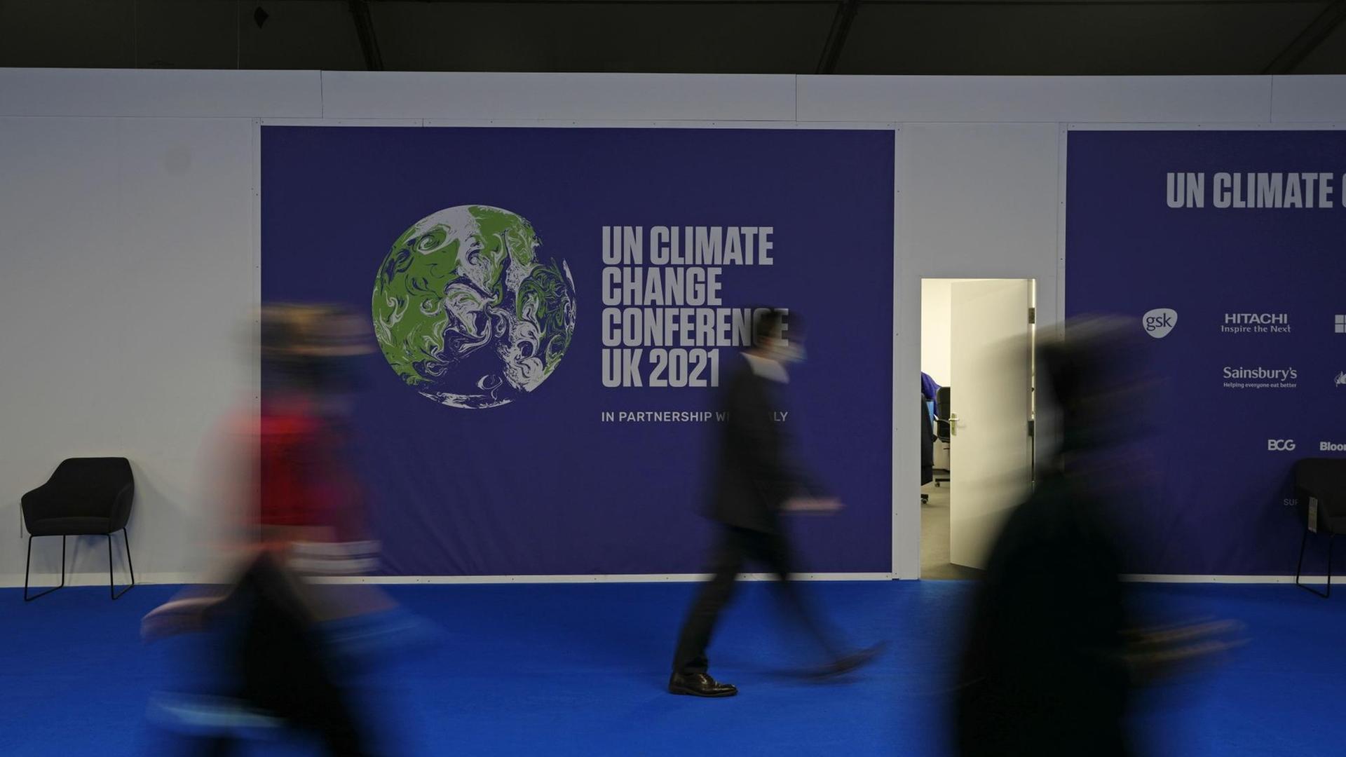 Ludzie chodzą przed banerem na Światową Konferencję Klimatyczną w Glasgow. 