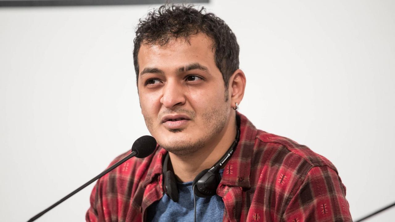 Galal Alahmadi sitzt bei einer Lesung an einem Tisch mit Mikrofon.