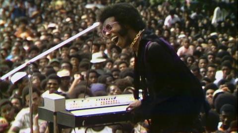 Sly Stone performt auf dem Harlem Cultural Festival, im Hintergrund ist das Publikum zu sehen.