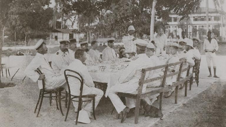 Weiß gekleidete Kolonialbeamte im damaligen Deutsch-Ostafrika sitzen um einen Tisch herum. Das Foto enstand im Jahr 1893. Weiß gekleidete Kolonialbeamte im damaligen Deutsch-Ostafrika sitzen um einen Tisch herum. Das Foto enstand im Jahr 1893.