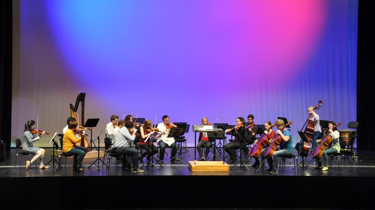 Junge Leute sitzen in einem Orchester auf einer bunt beleuchteten Bühne. Junge Leute sitzen in einem Orchester auf einer bunt beleuchteten Bühne.