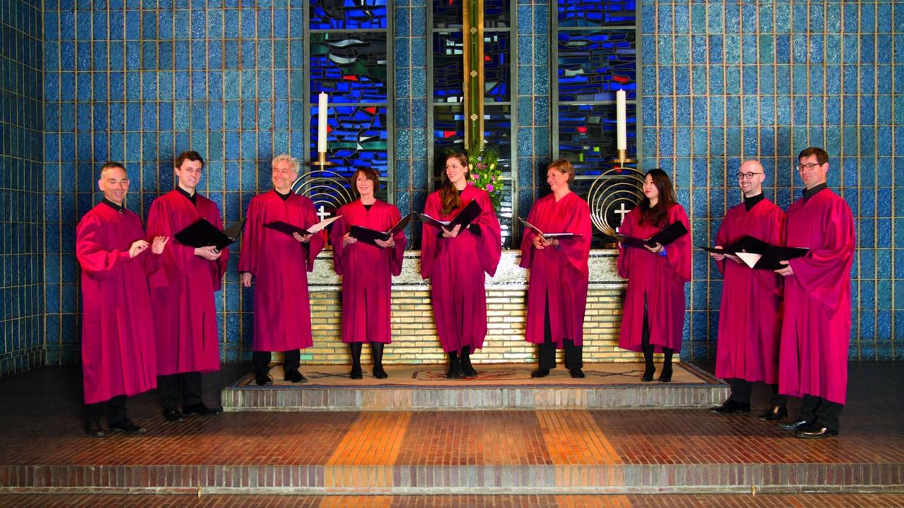 Neun Sänger stehen in langen roten Roben an einem modernen Altar.