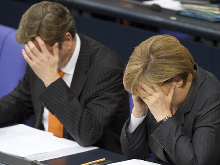 Außenminister Guido Westerwelle (FDP) und Bundeskanzlerin Angela Merkel (CDU) sitzen in Berlin im Bundestag und halten sich die Hände an den Kopf.