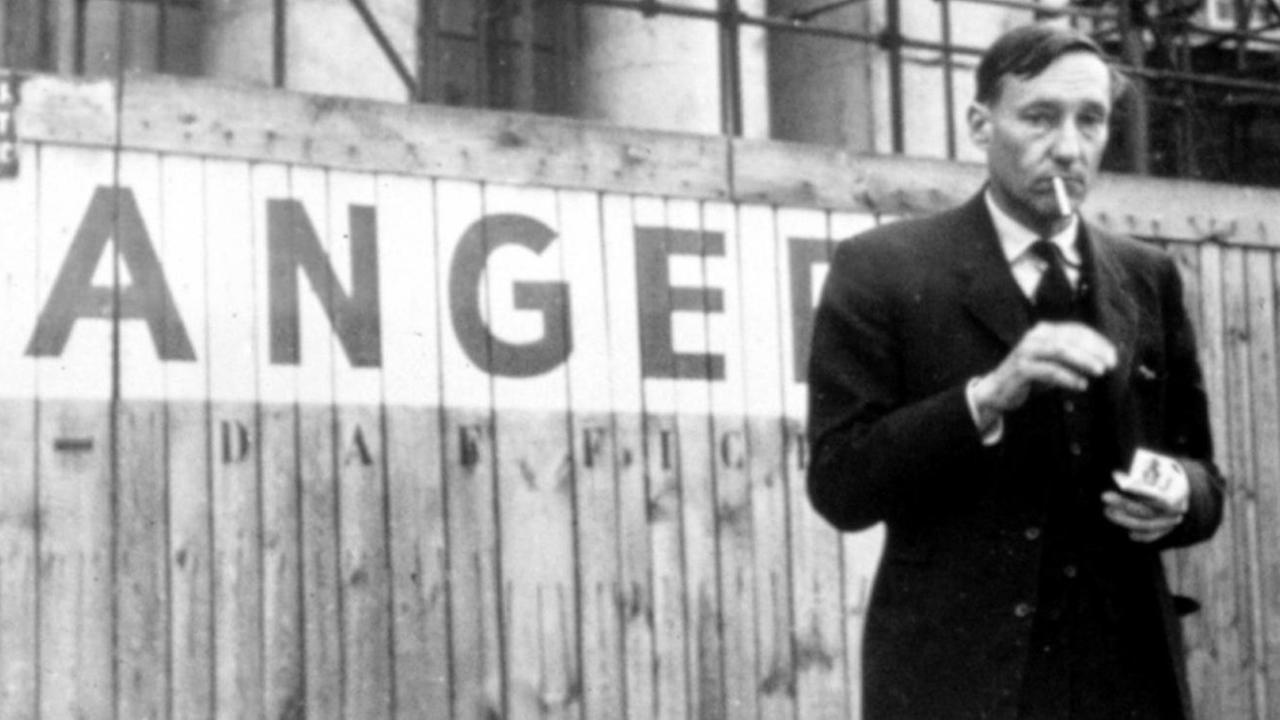 William S. Burroughs steht rauchend an einem Bauzaun