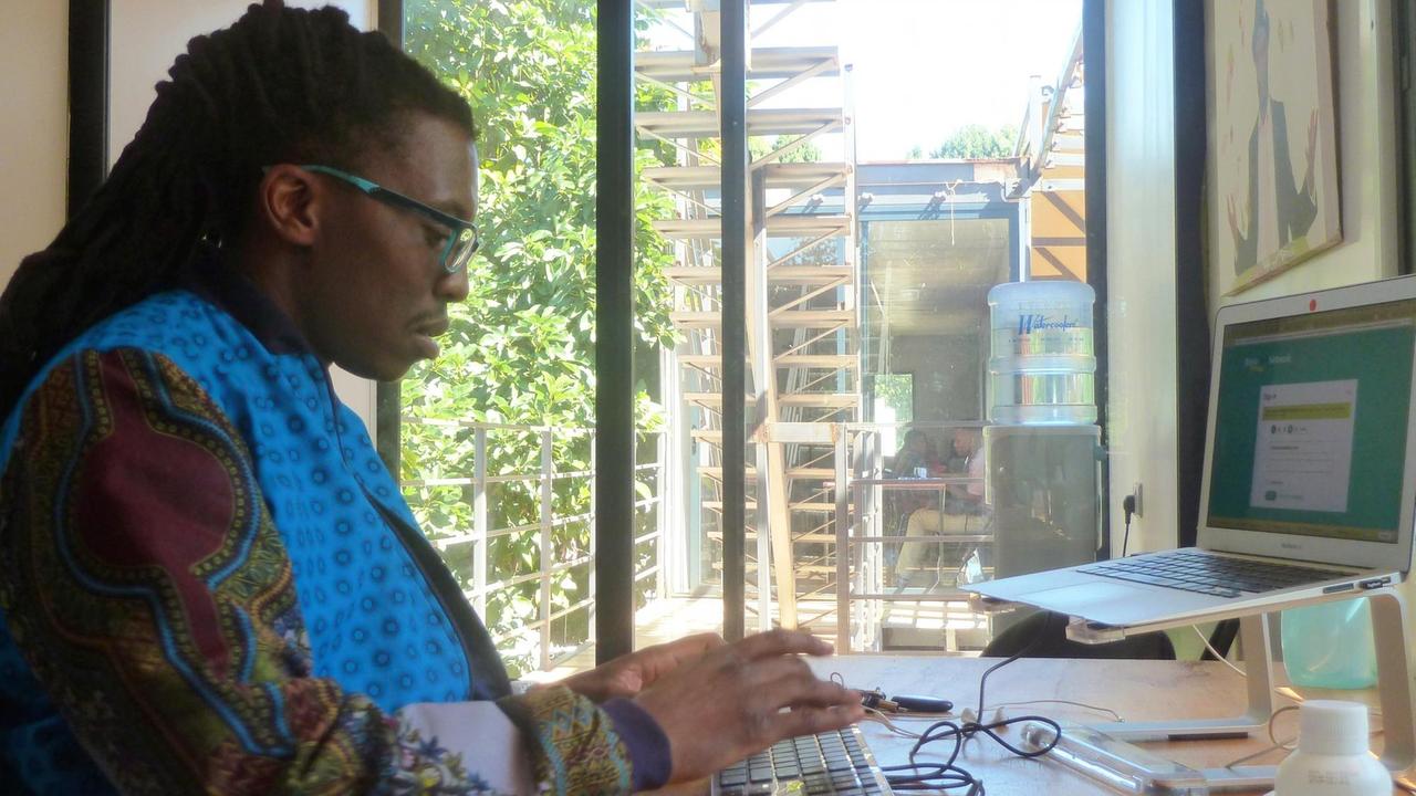 Tongai Makawa alias Outspoken sitzt mit Laptop am Schreibtisch in seinem Büro im Kreativzentrum "Moto-Republik"