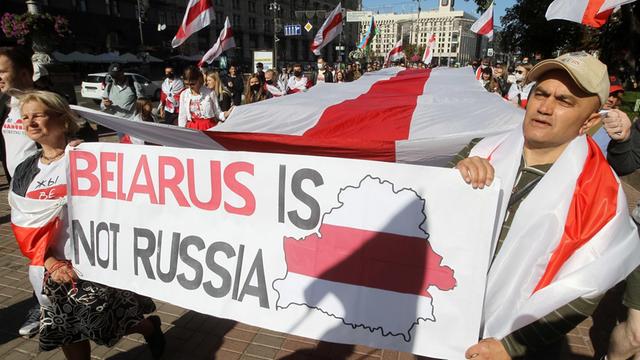 Protestanten halten die rot-weiße Flagge von Belarus während einer Demonstration in Kiew, auf einem Plakat steht: "Belarus is nor Russia"