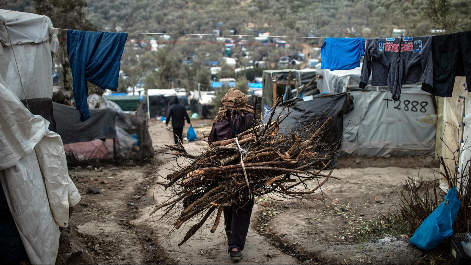 Ein Flüchtling trägt Holz auf dem Rücken, in einem provisorischen Lager neben dem Lager in Moria. Ein Flüchtling trägt Holz auf dem Rücken, in einem provisorischen Lager neben dem Lager in Moria.