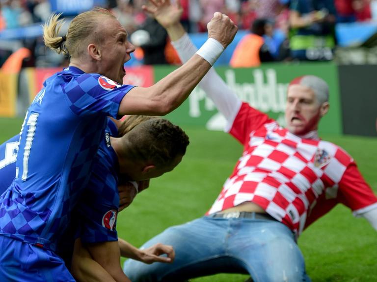 Vida und die anderen beiden Spieler umarmen sich jubelnd am Spielfeldrand. Im Hintergrund rutscht der kroatische Fan auf den Knien heran.